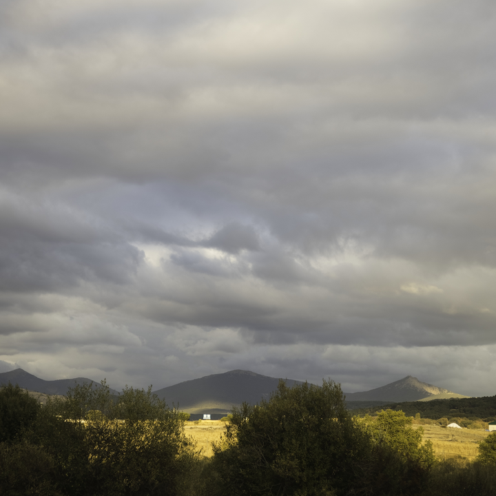  Scenic view of the rural landscape near El Espinar, Segovia, Spain, during autumn. Sunlight pierces through heavy clouds, illuminating the fields and distant mountains in soft golden tones. October 2025. 