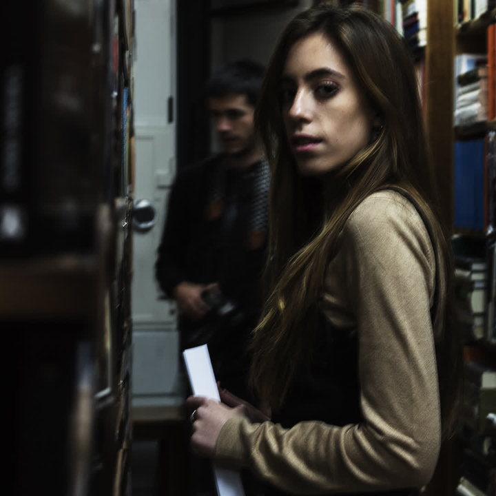 A young woman stands thoughtfully in a quaint bookshop, browsing through shelves filled with books. The warm and quiet atmosphere invites exploration and discovery. 