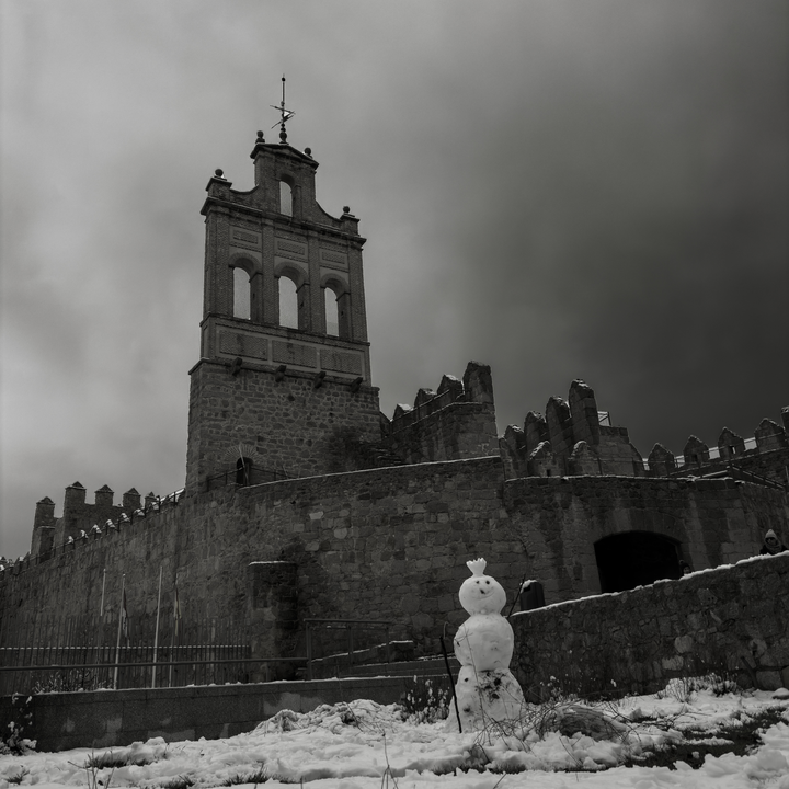 A snowman built in front of the historic Arco del Carmen gateway and the medieval stone rampart walls of Avila, Castile and Leon, Spain, during a cold and snowy winter day.