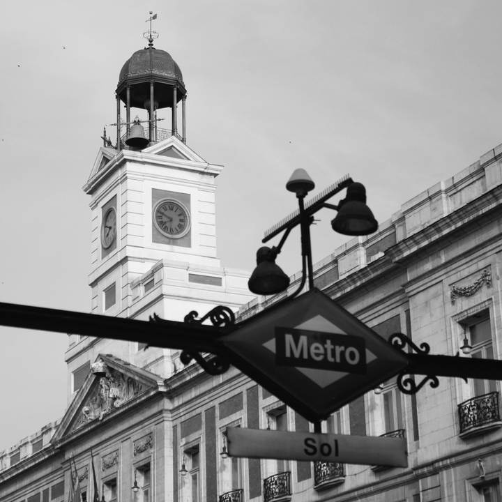  Classic black and white photo of the iconic Puerta del Sol Metro sign with the historic clock tower behind, capturing the spirit of central Madrid and its architectural charm. 