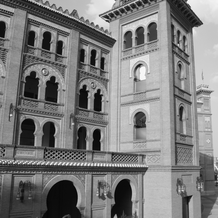  Striking black and white photograph of Las Ventas, Madrid's iconic bullfighting arena, highlighting the intricate Neo-Mudéjar design and elaborate brickwork details under soft daylight. 