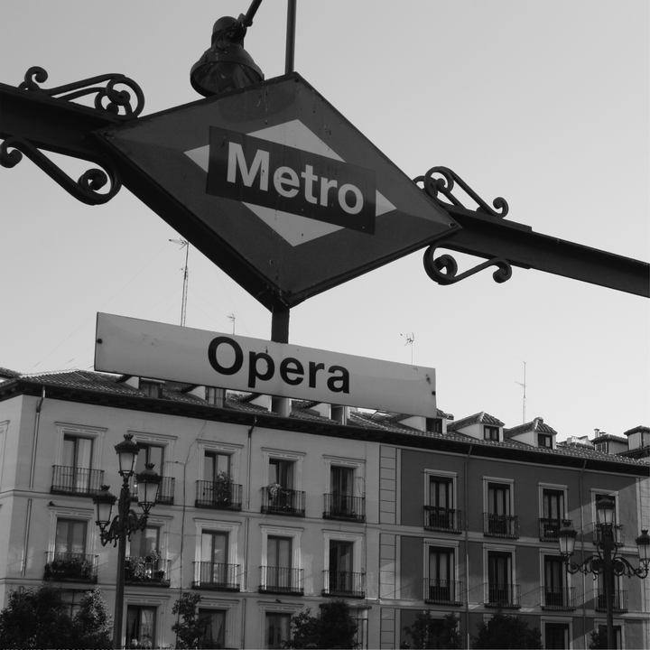  Madrid's Opera Metro station sign at street level, framed by grand classical buildings and evocative European ambience. 