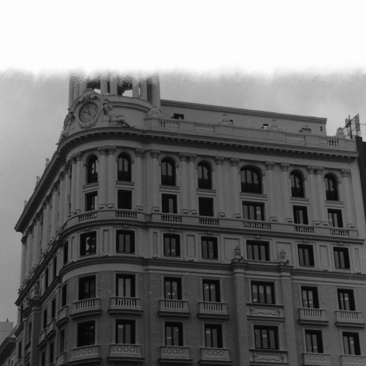 Atmospheric monochrome photograph of a grand classical building in Madrid, featuring ornate facades, arched windows, balconies, and a decorative clock tower—capturing the city’s historic charm and cultural heritage.